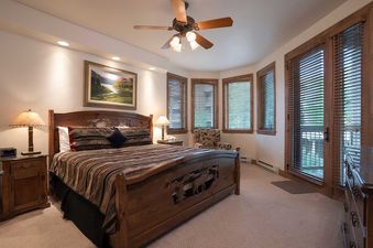The master bedroom in Chateau Chamonix CX336 features a large wooden bed, a bay window with an armchair, and a door leading to a balcony, all under recessed lighting and a ceiling fan.