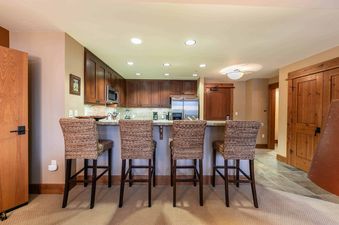 A kitchen with four bar stools and a stainless steel refrigerator