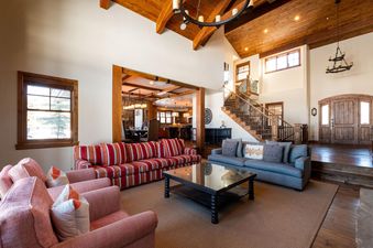 A spacious great room at Snowtop Manor with high ceilings, exposed wooden beams, a large chandelier, and two comfortable sofas.