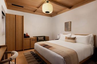 A modern bedroom with a large bed, wooden furniture, and a ceiling with exposed wooden beams.