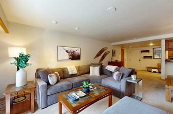 A cozy and inviting living room at Fallridge 204 featuring a large grey sectional sofa, a wooden coffee table with stone inlay, and a framed artwork of a longhorn bull.