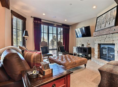 A cozy living room in Silver Star 903 with a fireplace, comfortable leather furniture, and a large window looking out onto trees.