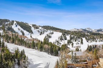 A panoramic winter wonderland awaits at St Regis 2 Bedroom Mountain View, offering breathtaking views of snow-covered mountains, evergreen forests, and ski slopes under a clear blue sky.
