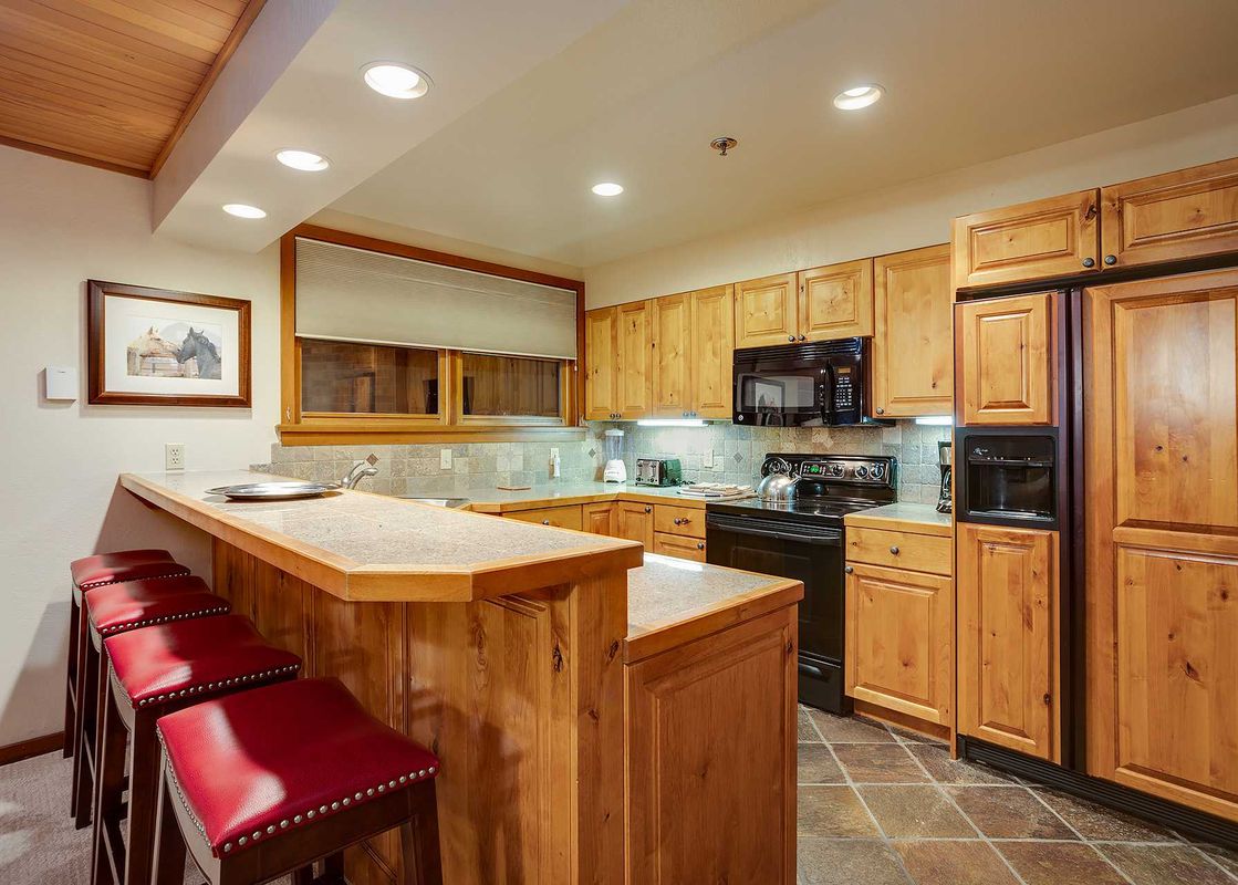 The image shows the Chateau Chamonix CX123 kitchen with wooden cabinets, black appliances, a breakfast bar with red stools, and tiled flooring.