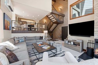A modern and cozy living room in Ridgepoint Townhome 166 with a grey sectional, stone fireplace, and elevated dining area.