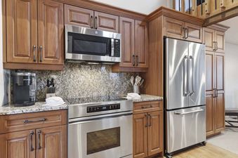 A modern kitchen with light brown wooden cabinetry, granite countertops, stainless steel appliances, and a Keurig coffee maker in Ridgepoint Townhome 090.
