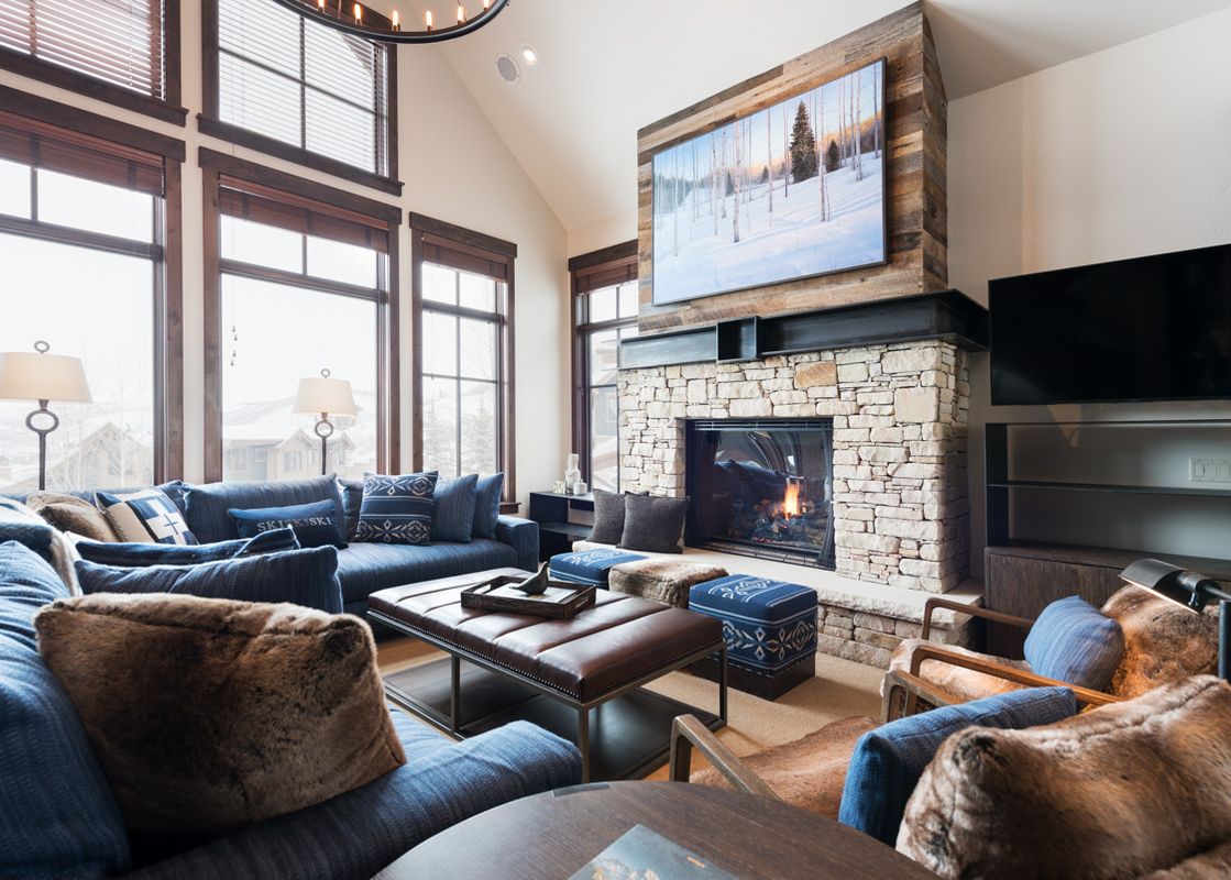 A spacious and elegantly furnished living room in Silver Star 40, featuring a stone fireplace, comfortable blue seating, and large windows with a winter view.