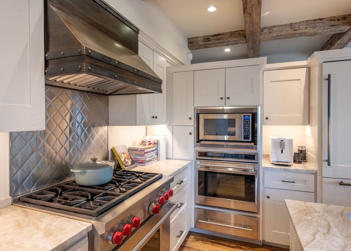 A modern kitchen with stainless steel appliances, white cabinets, and rustic wood ceiling beams in Shooting Star Cabin 05.