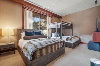 A cozy bedroom at Solaris 2A South featuring a king bed with a fur throw, a bunk bed, a nightstand with a lamp, and a large window with outdoor views.