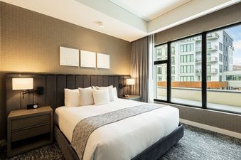A hotel room with a king-size bed, nightstands, and a large window with a view of the city.