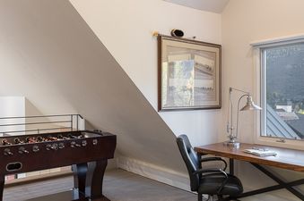 A sloped-ceiling attic room at the Serenvale Retreat features a foosball table and a desk with a lamp, chair, and mountain views.