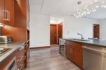 The Solaris 3BS features a sophisticated kitchen with dark wood cabinetry, a large kitchen island with a sink and modern faucet, and stainless steel appliances, all illuminated by a unique chandelier.