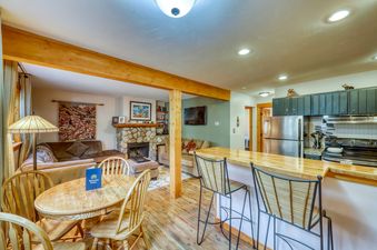 A living room and kitchen area with a fireplace in the living room and a stainless steel refrigerator in the kitchen.