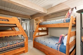 A bunk bedroom at Enclave 207 with two wooden bunk beds featuring colorful bedding and exposed ceiling beams.
