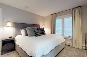 A luxurious bedroom at Chateau Christian 2 Bedroom Diamond Unit 120, featuring a king-sized bed with plush bedding, elegant nightstands with reading lamps, and large windows with privacy blinds and drapes.