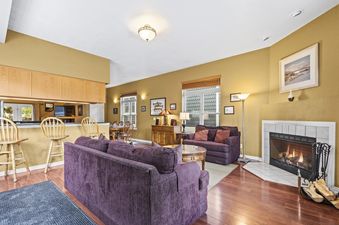 The Old Town Retreat features a spacious and inviting living area with plush purple sofas, a cozy fireplace, and an adjacent dining area, all bathed in natural light.