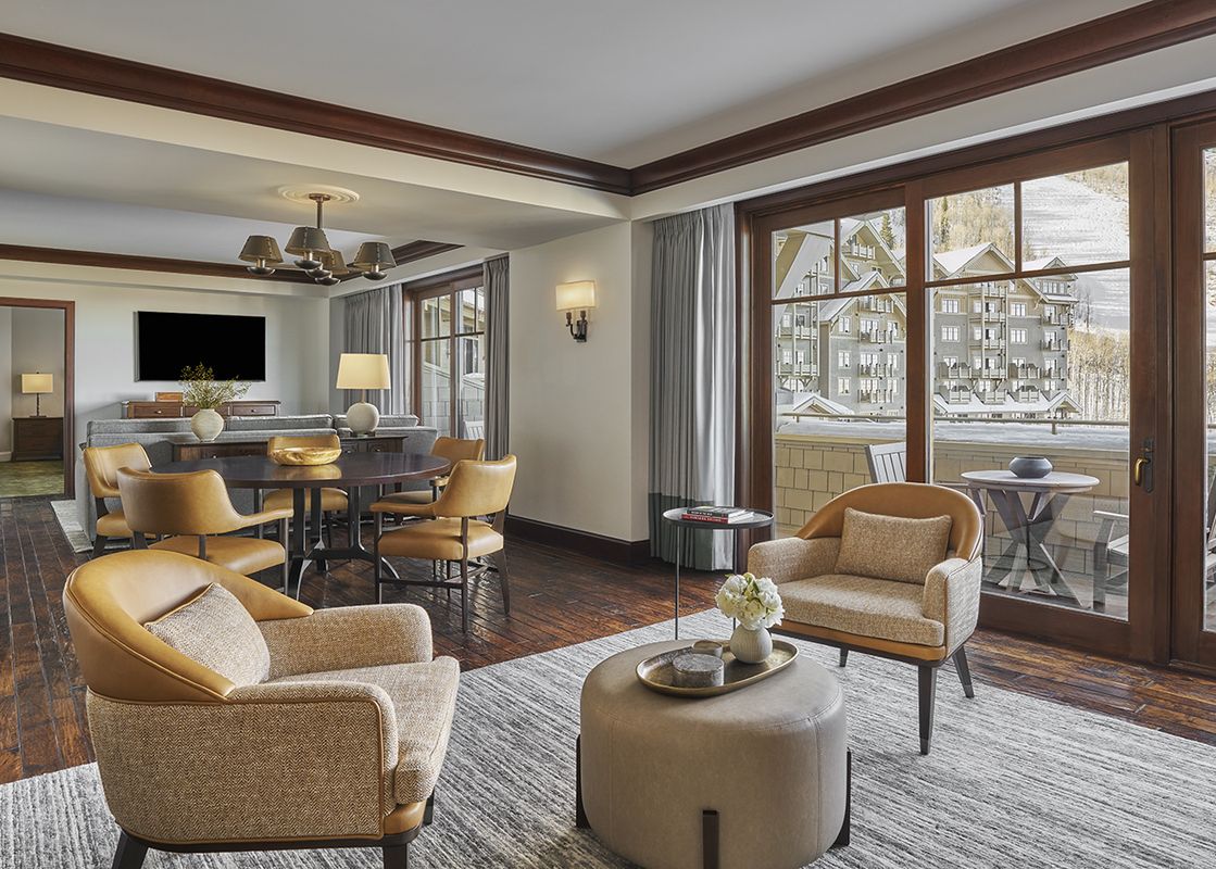 A spacious Montage Alpine Residential Suite features a comfortable living area with elegant furnishings, a dining space, and large windows revealing a snowy mountain landscape.