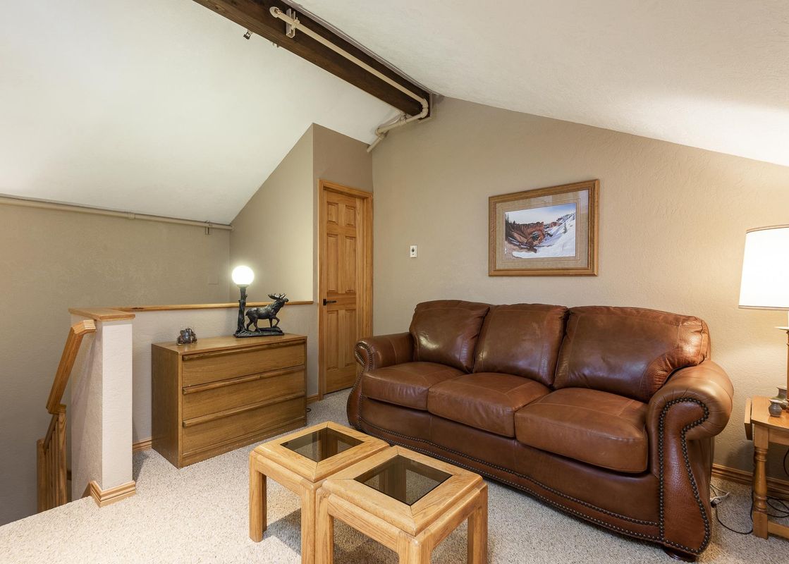 A cozy loft living area at Snow Flower 158 Park City featuring a brown leather sofa, wooden coffee tables, and rustic decor.
