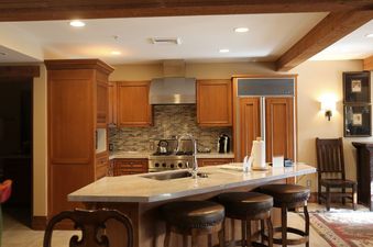The fully equipped kitchen in The Chateaux Deluxe Studio features stainless steel appliances, warm wooden cabinetry, and a large central island with bar seating.