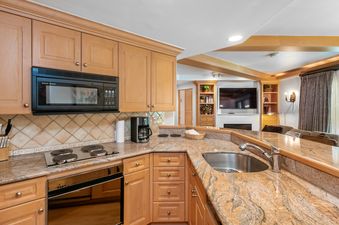The kitchen and living area of the unit are shown, featuring wood cabinetry, granite countertops, and modern appliances.