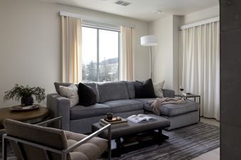 A modern living room with a gray sectional sofa, a coffee table with books, and a view of a snowy landscape through a large window.