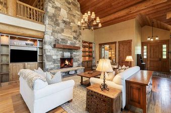 The living area of the Deer Valley Oak Lodge features a stone fireplace, comfortable sofas, and a rustic chandelier.