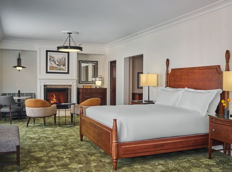 A spacious Montage Resort View Junior Suite with a comfortable bed, a cozy fireplace, and a dining area, all adorned with elegant furnishings and a patterned green rug.