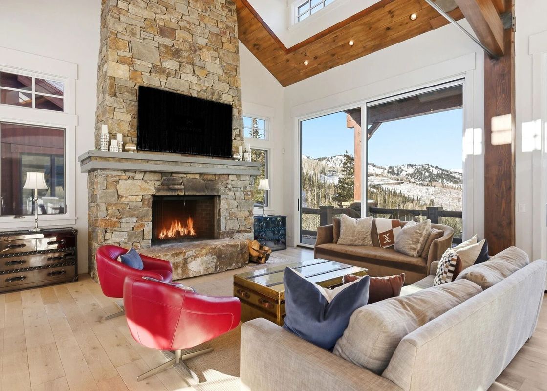 The light-filled living area of Snow Dance at The Colony featuring a stone fireplace, cozy sofas, and mountain views.