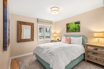 A serene bedroom at Dolomite Villas Unit 10 featuring a bed with a blue upholstered headboard, white bedding, a wooden nightstand with a lamp, a green-toned artwork, and a large mirror.