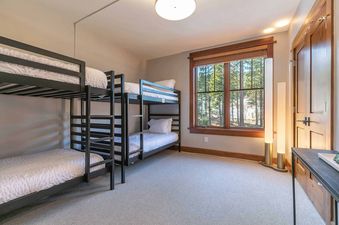 A bedroom with a bunk bed, a window with a view of trees, and a wooden door.