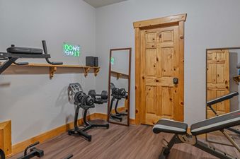 The gym at Starlit Pines Lodge has a weight bench, a pull-up bar, a dumbbell rack, a mirror and a neon sign that reads 'Don't Quit'