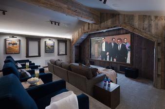 A luxurious home cinema at Northern Exposure with tiered seating, a large projection screen displaying a movie, and rustic wood accents.