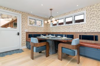 A dining nook with a round table, four chairs, a bench, and a window with an exterior view.