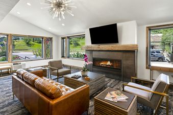 The contemporary living area of Torian Plum Plaza 202 features a fireplace, a mounted TV, and ample seating, with large windows overlooking a lush green landscape.