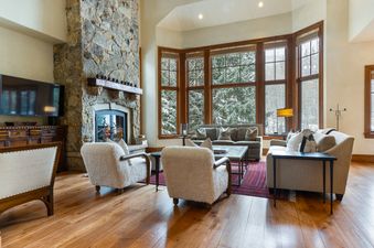 A large living room with a fireplace, a couch, and two chairs all facing a large window overlooking a snowy forest