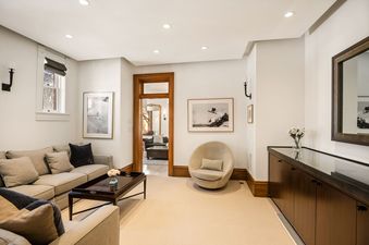 A serene lounge area at The Sardy House features plush sofas, a coffee table with flowers, a unique circular armchair, and elegant artwork on light-colored walls.