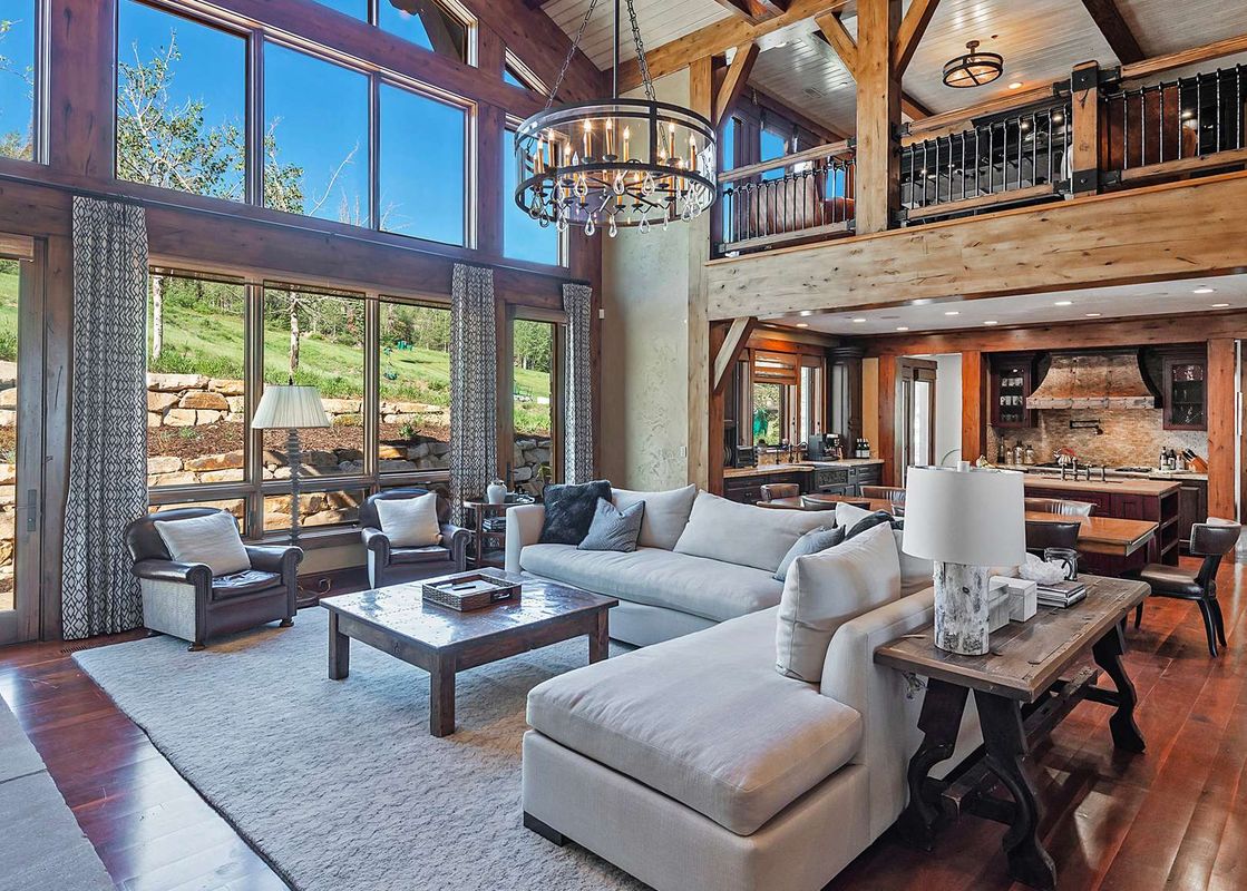 A luxurious living room features a large sectional sofa, a rustic coffee table, and an open-concept design with a kitchen in the background.