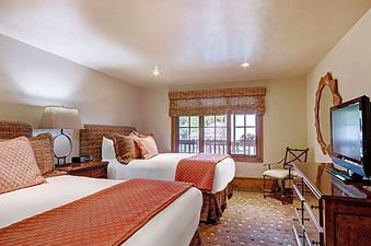 A cozy bedroom with two beds, a bedside table with a lamp, a window, and a TV on a dresser.