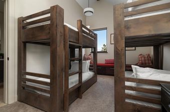Two sets of bunk beds in a room with a window nook and modern lighting.