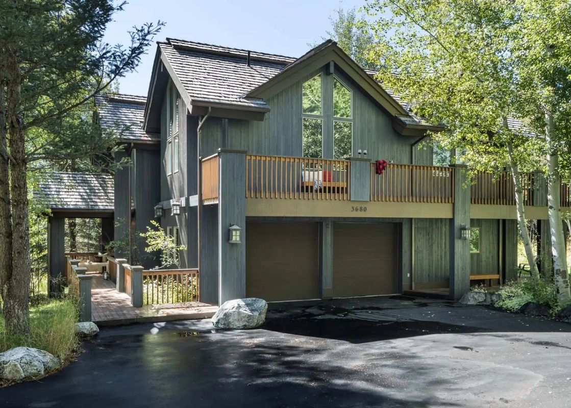Exterior view of Teton Grove with a wooden deck, a two-car garage, and lush green trees.