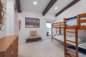 A cozy bunk room in Enclave 313 featuring a wooden bunk bed with white bedding and blue blankets, a framed mountain art piece, a bench, and a dresser.