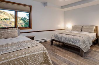 The secondary bedroom at Ranch at Steamboat RA605, featuring a bed with a patterned comforter, two pendant lights, and a window overlooking trees and hills.