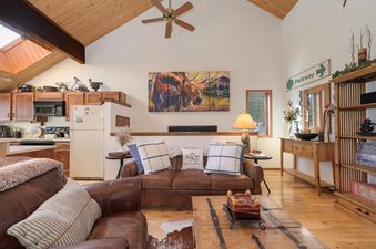 An open concept living area and kitchen with vaulted ceilings and rustic wood finishes.