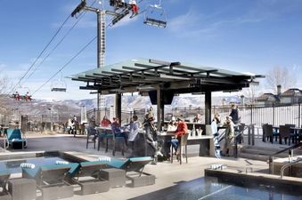 A large outdoor hot tub and pool area sits at the base of a ski lift, surrounded by mountain views.