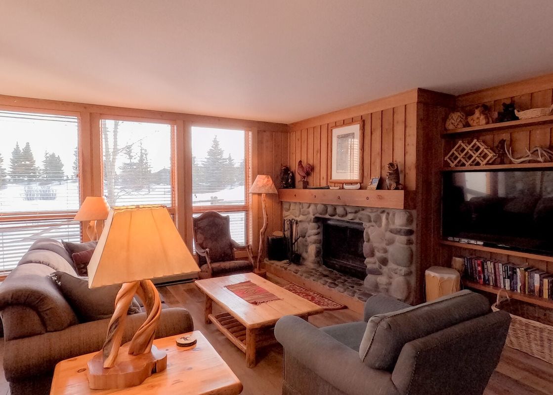 Cozy living room with stone fireplace, wood paneling, plush seating, and snow-filled forest views in Nez Perce D1.