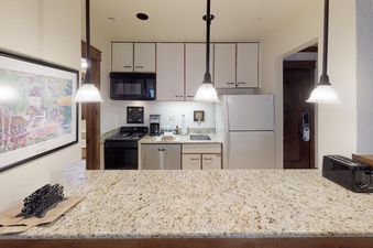 The kitchen in Manor Vail 285 features white cabinets, a full-size refrigerator, a stovetop, oven, dishwasher and a granite countertop.