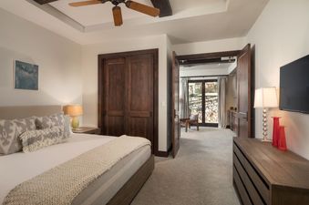 A bedroom in Lumiere Four Bedroom Residence with a king-sized bed, a white duvet, and a blanket, along with a dresser with several drawers, a lamp, and a TV on the wall.