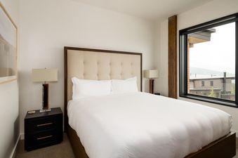 Moonlight Basin 201 Lakelodge features a bedroom with a king size bed, nightstands and lamps, and a large window with a view of the mountains