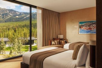 Modern and elegant bedroom featuring two queen beds and a large window overlooking a scenic pine forest and mountain range.