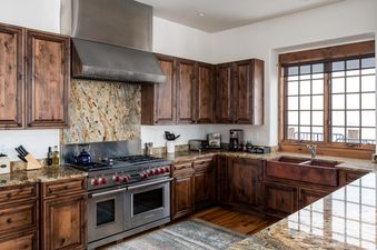 The kitchen in Moonlight Basin Luxury Suite 6A features stainless steel appliances, dark wood cabinetry, and granite countertops.